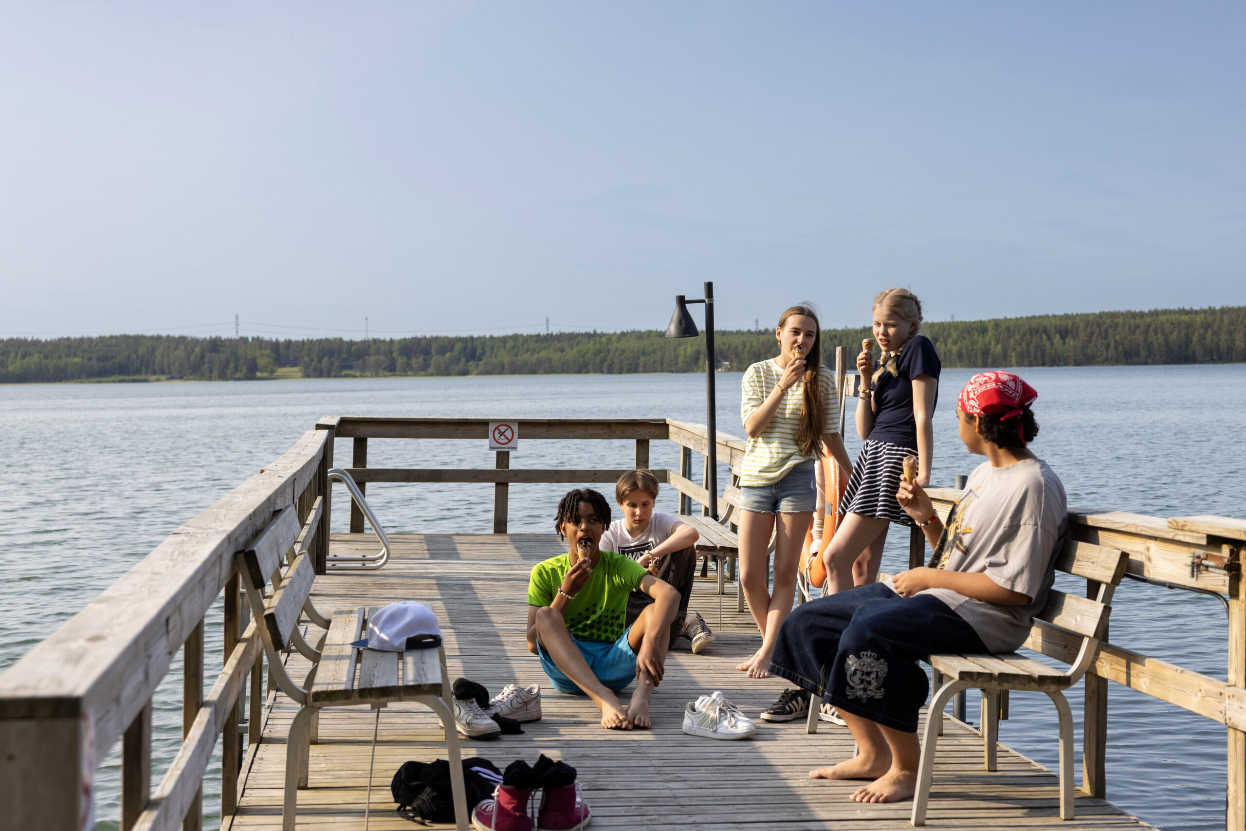 A group of young people smiling and talking on a swimming dock by a lake.
