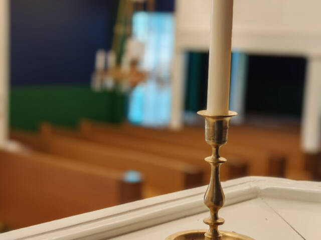 Lähikuva pitkästä kruununkynttilästä, taustalla kirkkosalia.