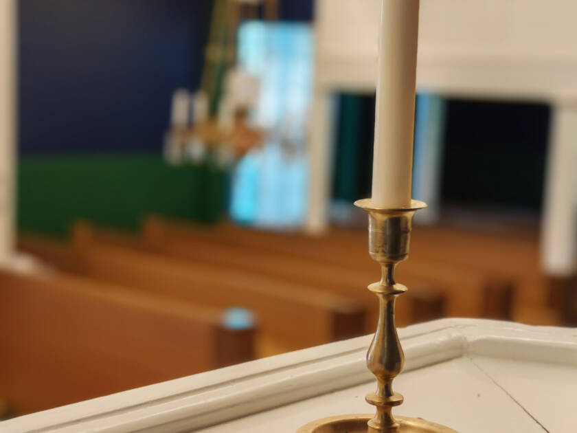 Lähikuva pitkästä kruununkynttilästä, taustalla kirkkosalia.