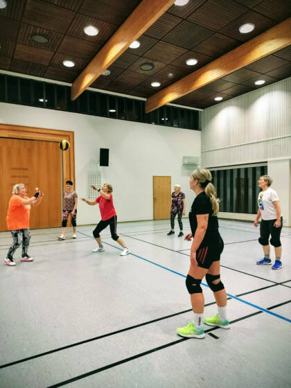 Naisia pelaamassa lentopalloa liikuntasalissa.