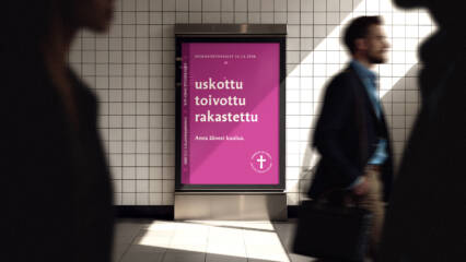 Jonkin julkisen tilan käytävällä sähköinen ilmoitustaulu, jolla näkyy kirkkaana seurakuntavaalien purppurapohjainen mainos ja kampanjansanat: uskottu, toivottu, rakastettu. Ilmoitustaulun ohi kulkee ihmisiä.