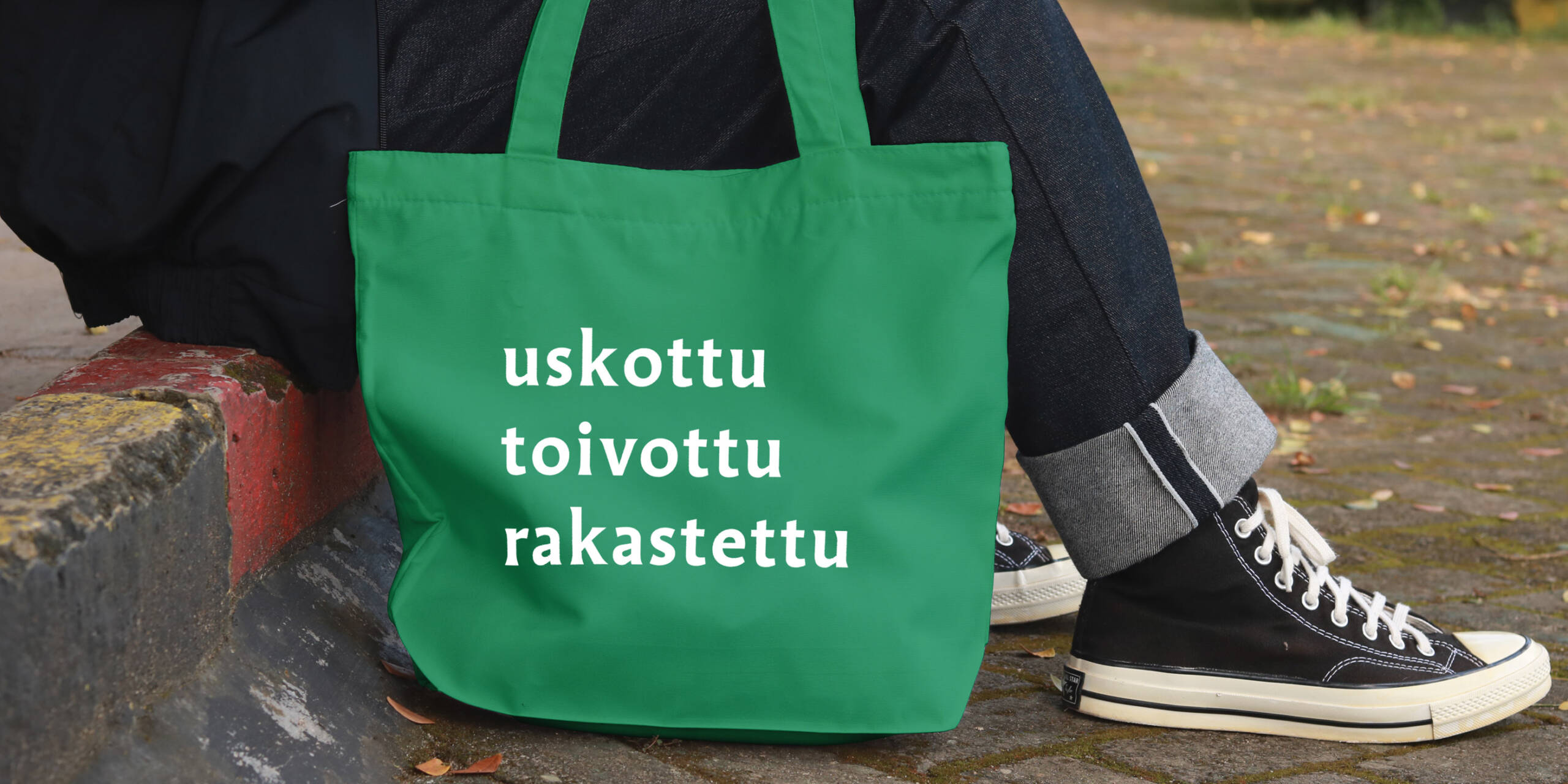 Istuvan ihmishahmon vieressä vihreä kangaskassi, jossa lukee kampanjasanat: uskottu, toivottu, rakastettu.