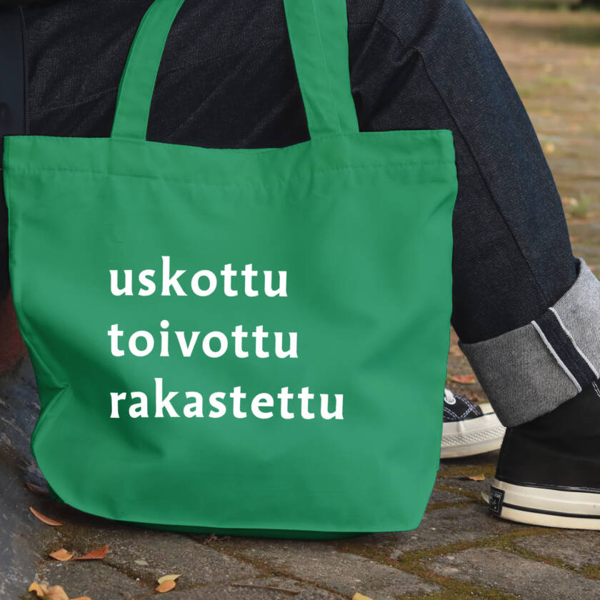 Istuvan ihmishahmon vieressä vihreä kangaskassi, jossa lukee kampanjasanat: uskottu, toivottu, rakastettu.