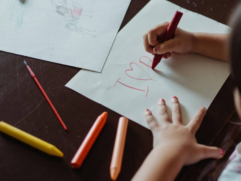 Yläviistosta kuvattuna lapsen kädet, jotka pitävät pöydällä paikoillaan paperiarkkia ja piirtävät sille kuvioita.
