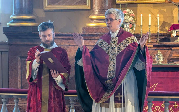 Liturgi tervehtii seurakuntaa punaisessa messukasukassa alidiakoni vierellään.