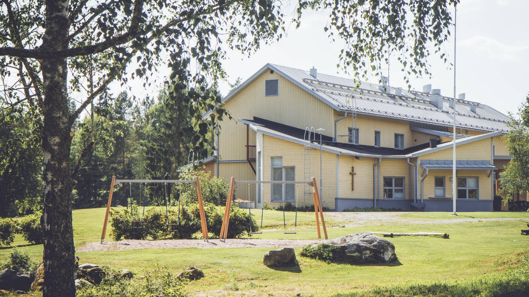 Pyysalo - keltainen iso puutalo iltapäivän auringossa. Etualalla leikkikenttä.